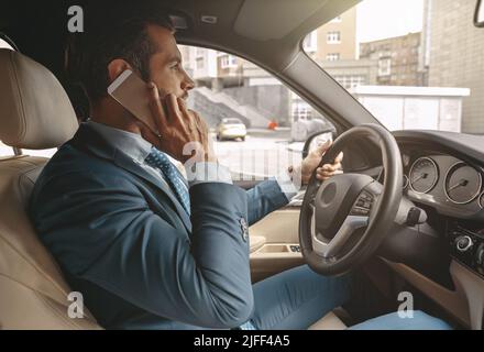 Taille nach oben Seitenansicht Porträt eines hübschen kaukasischen Mannes, der auf dem Handy spricht, während er ein Auto fährt Stockfoto