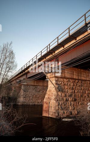 Eine vertikale Aufnahme einer Brücke in der Sommerlandschaft, die während des Sonnenuntergangs von einem See und Bäumen umgeben ist Stockfoto