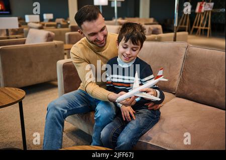 Hübscher junger Mann aus dem Nahen Osten, liebevoller Vater, der mit seinem entzückenden Sohn in der VIP-Lounge des internationalen Flughafens Spielzeug spielt Stockfoto