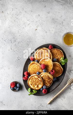 Pfannkuchen mit frischen Beeren und Honig auf ovalem Teller auf grauem Hintergrund mit Textraum, flach Lay Frühstück Zusammensetzung Stockfoto