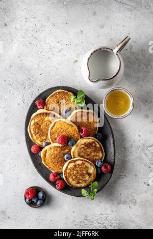 Pfannkuchen mit frischen Beeren und Honig auf ovalem Teller auf grauem Hintergrund, Draufsicht Stockfoto