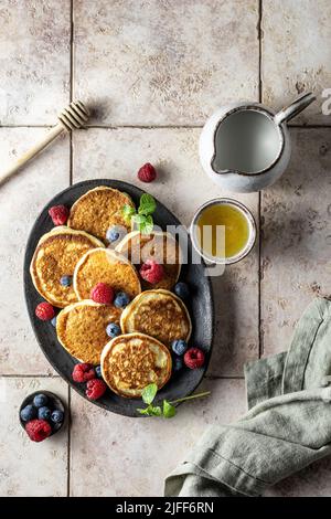 Pfannkuchen mit frischen Beeren, Honig und Leinenserviette auf rosa Fliesenhintergrund, flach liegend Stockfoto