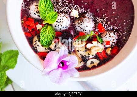 Köstliche Smoothie-Schale mit tropischen exotischen Früchten, Beeren, Samen, verziert mit Orchideen und grüner Minze. Das Konzept der gesunden Ernährung. Flatlay. Stockfoto