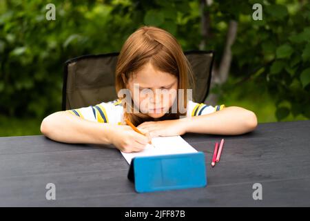 Online-Fernunterricht. Schulkinder mit Telefon mit Videokonferenz-Chat mit Lehrer und Klassengruppe. Das Kind lernt im Garten. Stockfoto