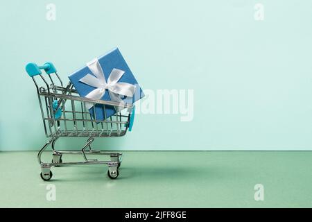 Schöne blaue Geschenkbox in Bändern in einem Warenkorb verpackt. Konzept des Online-Shoppings auf der ganzen Welt. Vorderansicht auf hellem Hintergrund. Stockfoto