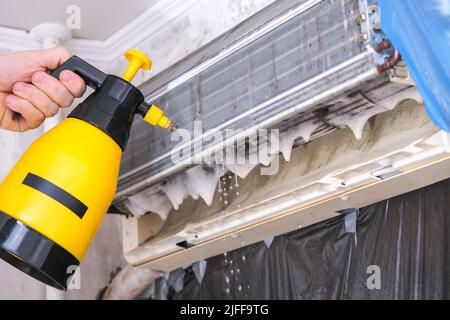 Ein Mann wäscht einen speziellen Schaum ab, um Klimaanlagen mit einem Wasserstrahl unter Druck zu reinigen. Wartung des geteilten Systems. Stockfoto