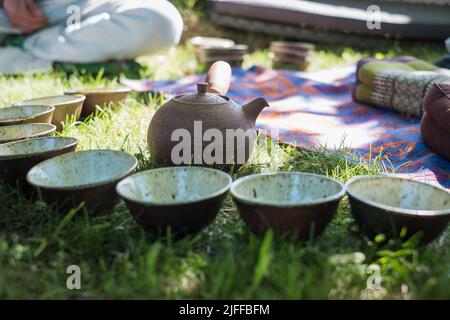 Teezeremonie im Sommer in der Natur. Handgefertigten Keramik-Teeschalen und Tontopf. Teekreis im Freien. Ruhige und entspannende Meditationstradition. Stockfoto