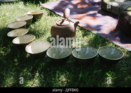 Teezeremonie im Sommer in der Natur. Handgefertigten Keramik-Teeschalen und Tontopf. Teekreis im Freien. Ruhige und entspannende Meditationstradition. Stockfoto