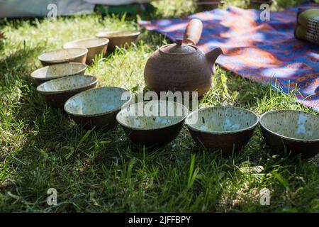 Teezeremonie im Sommer in der Natur. Handgefertigten Keramik-Teeschalen und Tontopf. Teekreis im Freien. Ruhige und entspannende Meditationstradition. Stockfoto