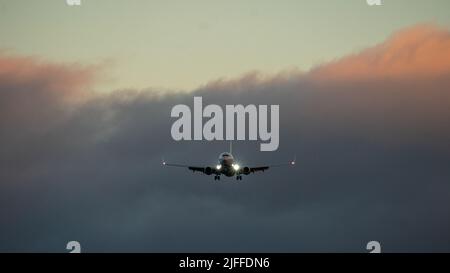 Die Silhouette eines Passagierflugzeugs, das vor dem Hintergrund des Sonnenuntergangs landet. Stockfoto