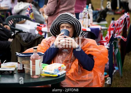 Woodstock, Oxfordshire, Großbritannien. 2.. Juli 2022. Frau trinkt Kaffee im Einweg-Regenponcho. Battle Prom Picknick-Konzerte. Blenheim Palace. Vereinigtes Königreich. Quelle: Alexander Caminada/Alamy Live News Stockfoto