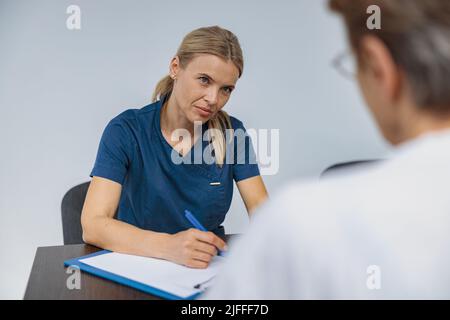 Der fokussierte Arzt füllt das Formular für medizinische Berichte über die medizinische Versorgung von Patienten während der Verabredung aus Stockfoto