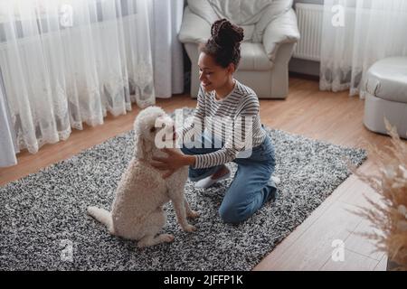 Draufsicht auf Mixed-Race ziemlich fröhliche weibliche chillen im Wohnzimmer spielen mit Haustier Stockfoto