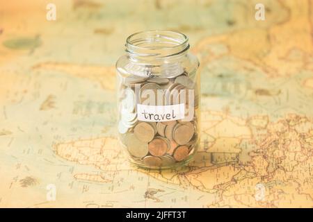 Glas mit Münzen und Reiseinschrift auf der Weltkarte auf dem Tisch. Reisekonzept und Geld sparen. Stockfoto