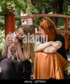 Glückliche Frau mit Ingwerhaar und Freund in einem gepflegten Park oder Garten. Unterstützung und gesunde Lebensweise. Weibchen mit Katze in ihrer 40s, die sich im Freien ausruhte Stockfoto