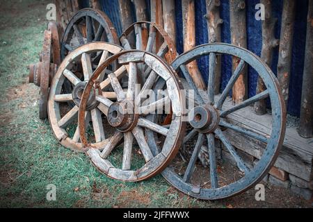 Antike Holzkarren Räder stehen auf der Straße auf dem Rasen in der Nähe der alten Scheune auf dem Gebiet des Haushalts im Dorf im privaten Sektor Stockfoto