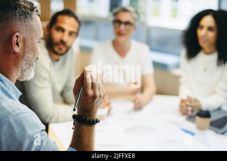 Ein reifer Geschäftsmann, der während eines Meetings mit seinem Team diskutiert. Gruppe von innovativen Design-Profis, die kreative Ideen während der Arbeit austauschen Stockfoto