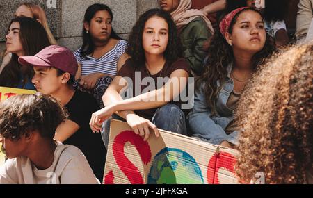 Verschiedene Jugendaktivisten, die vor einem Gebäude mit einem Banner „Unsere Spezies retten“ sitzen. Gruppe multikultureller junger Menschen, die gegen den globalen Krieg protestieren Stockfoto