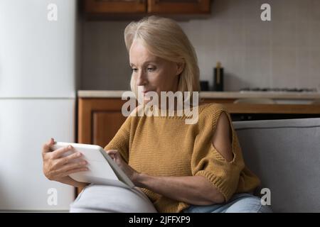 Ältere Frau, die zu Hause ein digitales Tablet benutzt, das auf der Couch sitzt Stockfoto