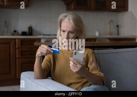 Beunruhigte Frau mit Karte und Handy, die Probleme mit E-Payment hatte Stockfoto