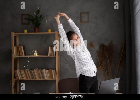 Unglückliche junge Geschäftsfrau, die unter Rückenschmerzen leidet, Probleme nach langen Stunden sitzender Arbeit, frustrierte verärgerte Frau Angestellte, die dabeisteht Stockfoto