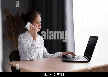 Seriöse hispanische Geschäftsfrau mit Laptop-Computer im Gespräch auf dem Mobiltelefon Kundenberater sitzen am Schreibtisch, fokussierte weibliche Verkaufsleiterin machen Zelle Stockfoto