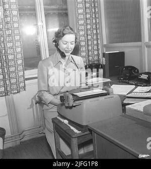 Büromädchen in den 1950s. Eine Frau sitzt vor ihrer Schreibmaschine in einem Büro und tippt etwas in Kopien. Sie hat ein Headset an und hört sich möglicherweise eine Aufzeichnung eines Briefes oder einer Nachricht an, die Sie eingeben möchten. Schweden 1955. Kristoffersson BM71-12 Stockfoto