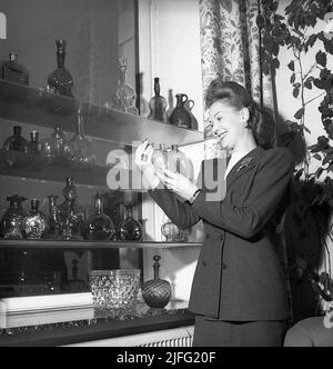 Einkaufen in der 1940s. Schauspielerin Greta Gynt, 1916-2000 im Laden Svenskt Tenn in Stockholm abgebildet mit Regalen von dekorativen Artikeln zum Verkauf. Der Shop ist hoch spezialisiert und berühmt für seine Kollektionen von dekorativem Design, die sie selbst produzieren und Importe aus der ganzen Welt. Svenskt Tenn ist immer noch im Geschäft (2022) Schweden 1946 Ref X122-4 Stockfoto