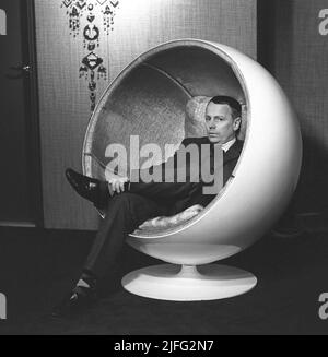 Inneneinrichtung des 1960s. Der Ball Chair wurde 1963 vom finnischen Möbeldesigner Eero Aarnio entworfen. Der Ball Chair ist auch als Globe Chair bekannt und ist bekannt für seine unkonventionelle Form. Es gilt als ein Klassiker des Industriedesigns. Das Bild, das in einer finnischen Möbelausstellung und dem Mann auf dem Stuhl aufgenommen wurde, ist NICHT Aarnio. 1967 Stockfoto