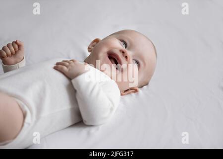 Glückliches Neugeborenes lacht, auf dem Bett liegend, Nahaufnahme Stockfoto