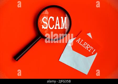 Scam Alert-Text auf Lupe und Notizblock auf rotem Deckelhintergrund. Konzept für Betrug und Betrug Stockfoto