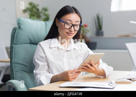 Eine schöne und erfolgreiche Geschäftsfrau arbeitet in einem modernen Büro, eine asiatische Frau nutzt einen Tablet-Computer. Stockfoto