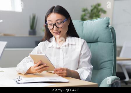 Eine schöne und erfolgreiche Geschäftsfrau arbeitet in einem modernen Büro, eine asiatische Frau nutzt einen Tablet-Computer. Stockfoto