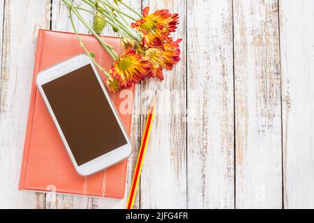 Frische Blume und Smartphone auf Notebook auf Holztisch Hintergrund Stockfoto