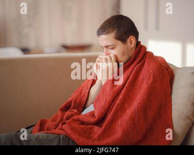Coronavirus. Kranker Mann mit Corona-Virus, der sich auf dem Sofa niederlegt und sich von einer Krankheit zu Hause erholt. Seine Nase bläst. Das Konzept der hohen Temperaturen. Die Person ist schwer krank. Stockfoto