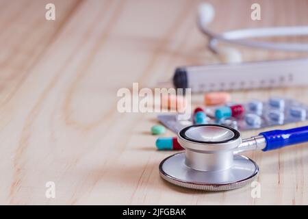 Nahaufnahme blaues Stethoskop und Tabletten mit Tabletten auf Holztisch. Gesundheit und medizinische Konzept Stockfoto