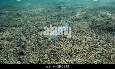 Aus der Nähe liegt eine Plastikflasche in den Sonnenstrahlen auf dem Meeresboden, im Küstenbereich am Strand. Plastikverschmutzung des Ozeans. Rotes Meer, Ägypten Stockfoto