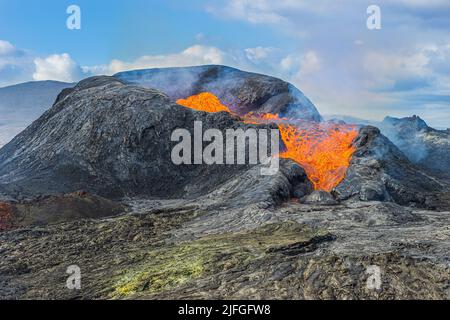Lavastrom aus einem Vulkankrater in Island. Aktiver Vulkan auf der Halbinsel Reykjanes. Landschaft bei Tag bei Sonnenschein mit Wolken und blauem Himmel. Gekühlt Stockfoto