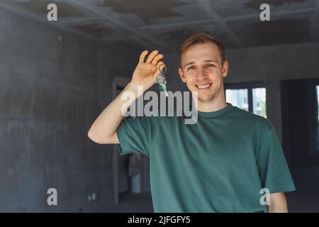 Konzentrieren Sie sich auf Schlüssel, die von begeisterten jungen, tausendjährigen Hausbesitzern gehalten werden. Glücklicher Einzelmann, der in einem neuen Haus zu Hause umzieht, Schlüssel vorführt und in apa steht Stockfoto