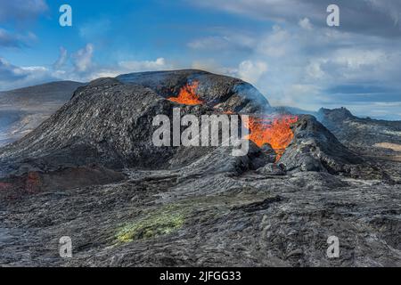 Aktiver Vulkan auf der isländischen Halbinsel Reykjanes. Landschaft im Frühling mit Sonnenschein. Flüssige Lava fließt aus der Seite des Krater. Wenig Dampf steigt auf Stockfoto