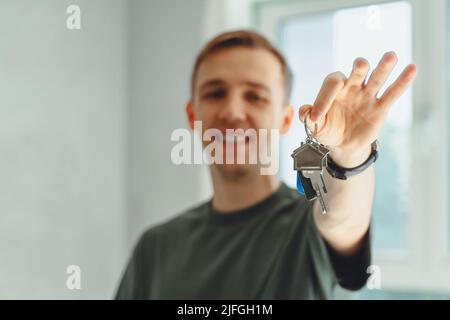 Konzentrieren Sie sich auf Schlüssel, die von begeisterten jungen, tausendjährigen Hausbesitzern gehalten werden. Glücklicher Einzelmann, der in einem neuen Haus zu Hause umzieht, Schlüssel vorführt und in apa steht Stockfoto