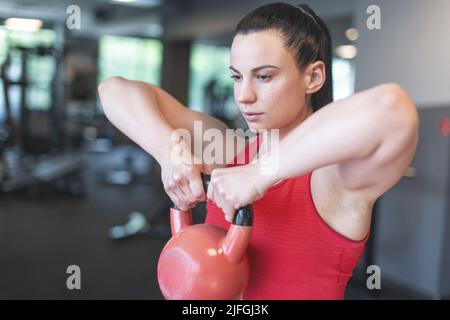 Junge kaukasische Frau, die im Fitnessstudio mit Kettlebell trainiert Stockfoto