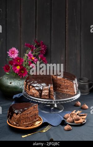 Eine Portion köstlicher hausgemachter dunkler Schokoladenkuchen Dessert mit Ganache-Glasur auf dem Kuchenständer über dunklem rustikalem Holzhintergrund Stockfoto