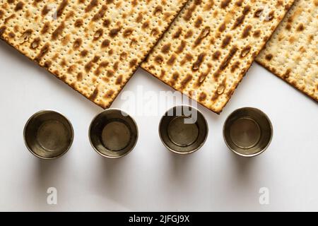 Drei Matzah Brot - Jüdisches Essen für Passah. Neben vier silbernen Cups.Draufsicht auf weißem Hintergrund Stockfoto