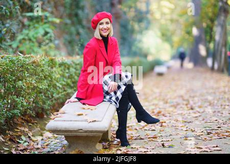 Lächelnde Frau, die im Herbstpark auf der Bank sitzt Stockfoto