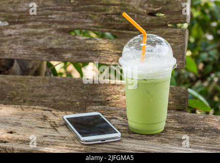 matcha Grüner Tee Smoothie Schlagsahne und Smartphone auf Holztisch Stockfoto