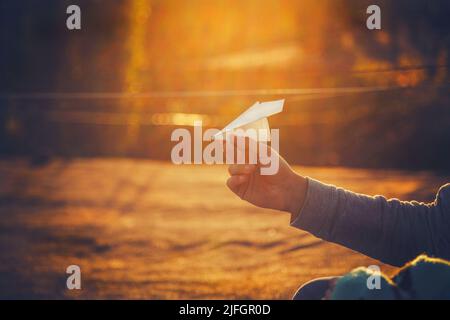 Papierflugzeug in der Hand des Menschen bei orangefarbenem Sonnenuntergang. Stockfoto