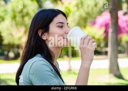 Brünette tausendjährige Frau trägt türkisfarbenen Tee im Stadtpark, im Freien trinken Kaffee zum Mitnehmen und Blick in die Ferne. Morgens im Freien. Stockfoto