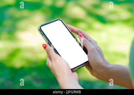 Junge, schöne Frau mit türkisfarbenem T-Shirt im Stadtpark, Hände im Freien, die ein Smartphone im Modell halten. Nahaufnahme. Stockfoto