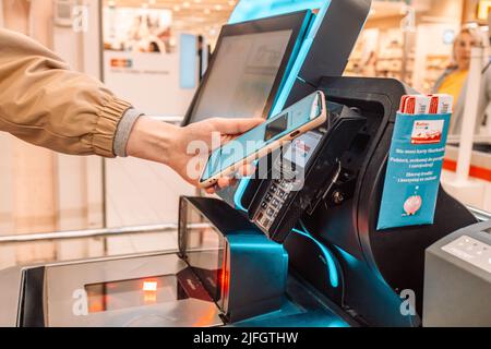 Krakau, Polen - 26. April 2022: Nahaufnahme schießen eine Frau Hand mit einem Smartphone zu zahlen mit bargeldlosen Brieftasche von E-Geld für POS-Kartenleser am Stockfoto